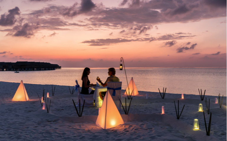 Couple is having a private event dinner on a tropical beach during sunset time.
