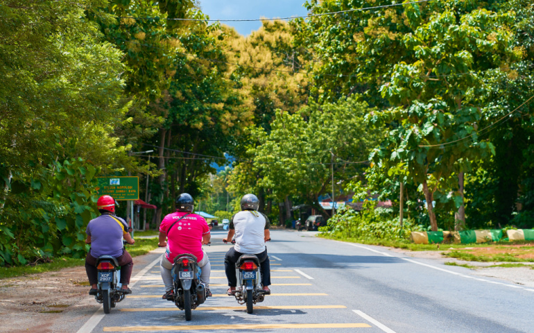 A company of three people ride motorbikes along the road in Langkawi