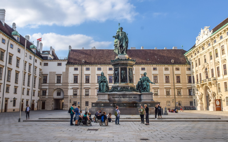 Wheel chair users take guided tour of Vienna tourist attractions and watch the Monument to Francis II in a courtyard at the Hofburg Palace