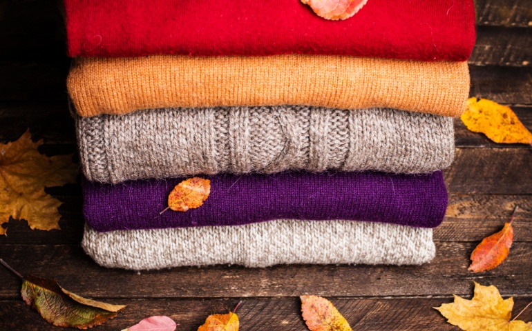 Pile of knitted winter clothes on wooden background 