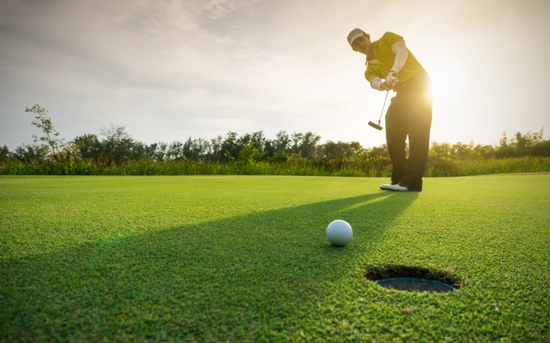 Golfer putting golf ball on the green golf. 