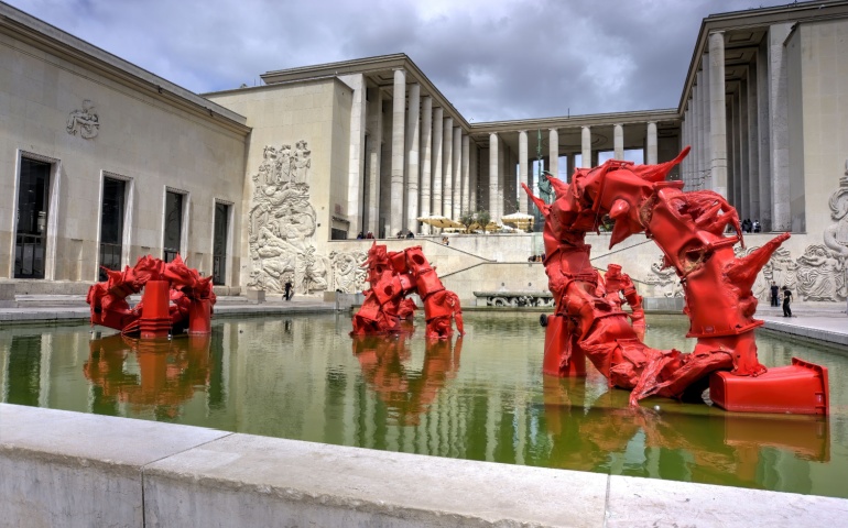 Exterior of Musee d'art Moderne De Paris with exhibit made from red wheelie bins in water feature.
