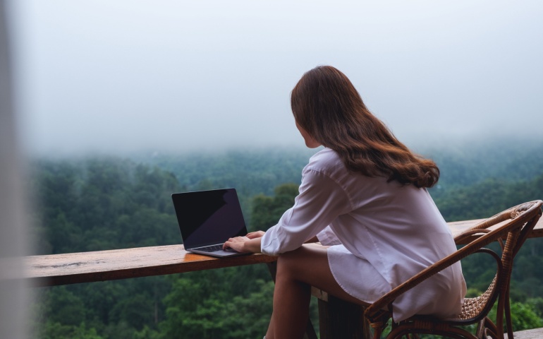 Woman working on her laptop with a scenic view in the background.