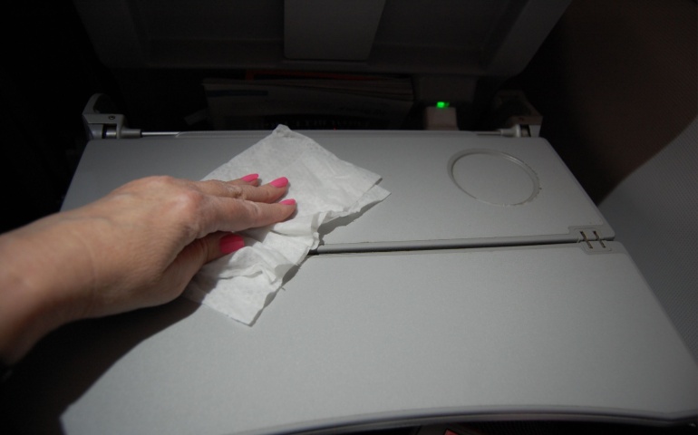 Airline passenger wipes sterilizes and disinfects the tray table on plane 